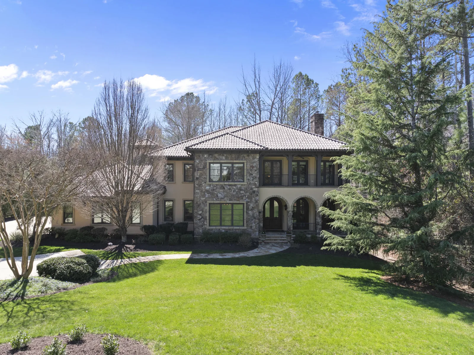 Custom Mediterranean-style home with a stone facade, tile roof and arched entry in a Triangle country club community