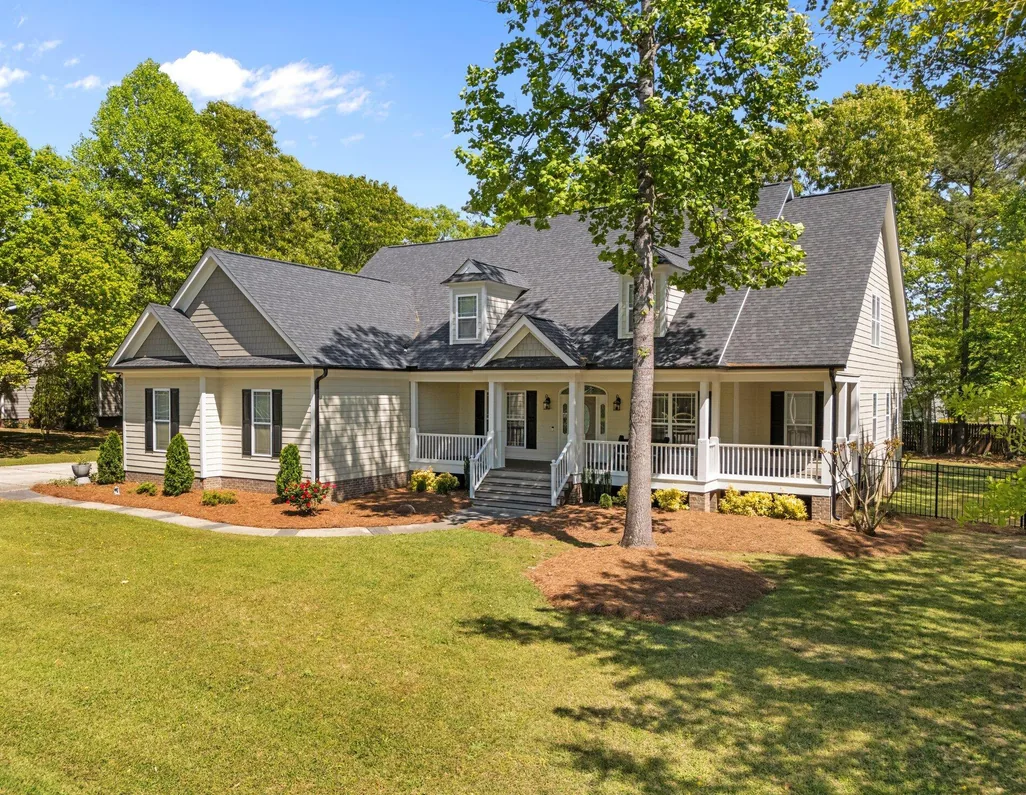 Light-colored home with a covered front porch, dormer windows and a large, private lawn